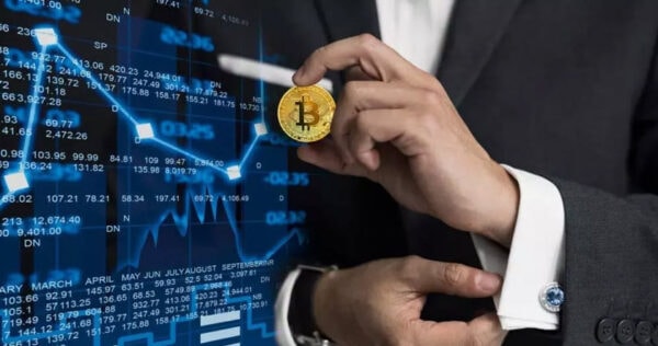 A person in a suit holds a Bitcoin coin in front of a digital financial chart displaying fluctuating stock data.
