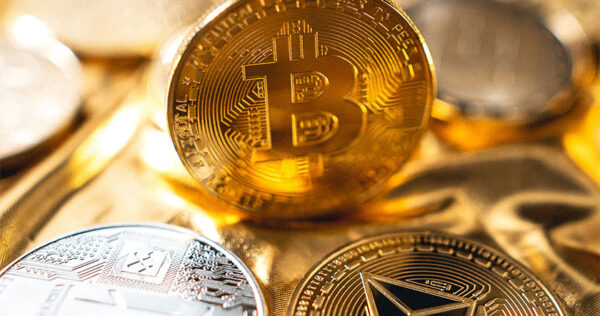 Close-up of assorted physical cryptocurrency coins, including Bitcoin and Ethereum, placed on a reflective golden surface.