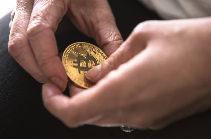 A person holding a physical representation of a Bitcoin coin between their hands.