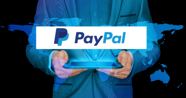 A person in a blue suit holding a tablet with the PayPal logo displayed over a digital world map background.