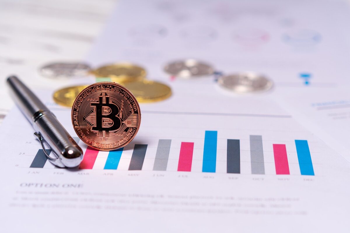 A Bitcoin coin, a pen, and coins are placed on a printed bar chart showing financial data.