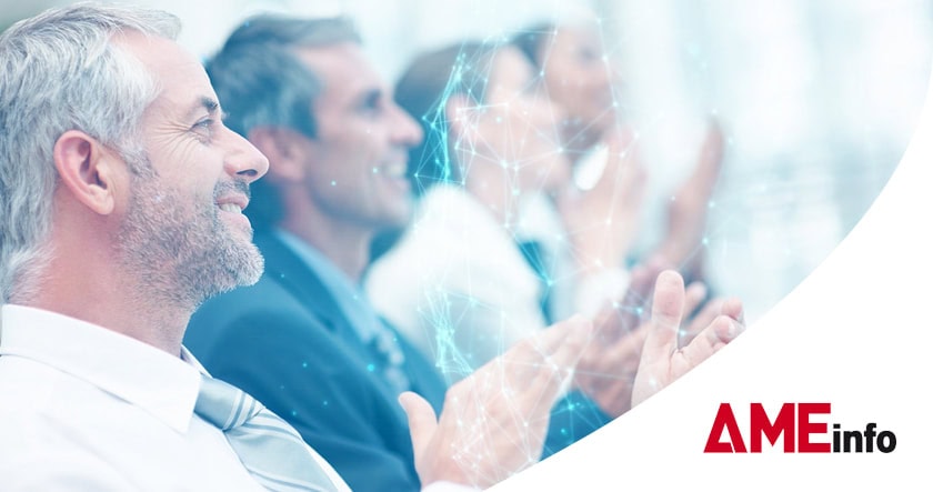 A group of people in business attire sit and applaud, with digital network graphics overlay and an "AMEinfo" logo in the corner.