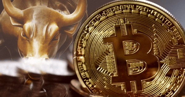 A close-up of a shiny Bitcoin coin in front of a bronze bull statue, symbolizing cryptocurrency and a bullish financial market.