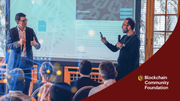 Two men stand in front of a screen presenting blockchain information to an audience at a Blockchain Community Foundation event.