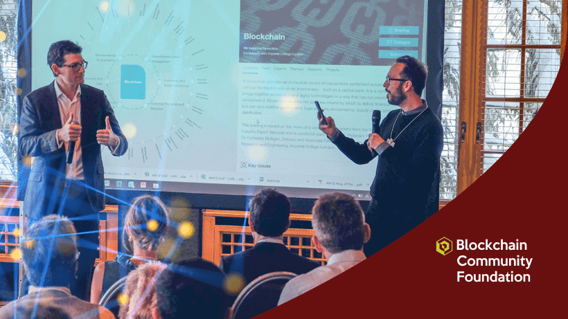 Two men stand in front of a screen presenting blockchain information to an audience at a Blockchain Community Foundation event.