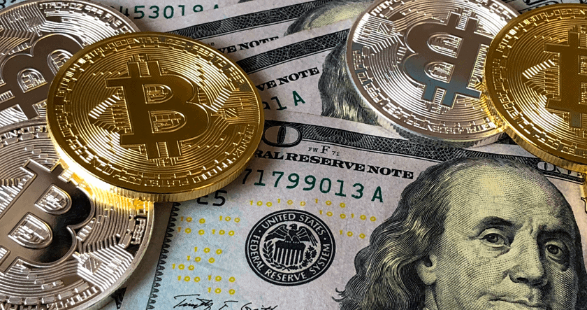 Gold and silver Bitcoin coins are placed on top of several one-hundred U.S. dollar bills.
