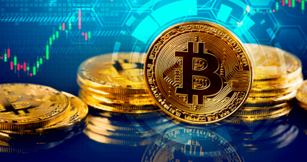 Stacks of gold-colored Bitcoin tokens are displayed in front of a digital background featuring a price chart and abstract technological graphics.