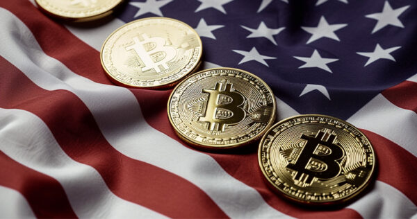Four gold Bitcoin coins are placed in a row on top of a fabric United States flag.