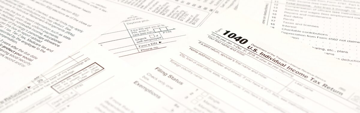 A close-up view of several U.S. tax forms, including a prominent 1040 Individual Income Tax Return form, scattered on a flat surface.