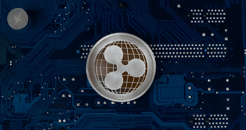 A silver Ripple (XRP) coin rests on a blue circuit board featuring electronic components and circuitry patterns.
