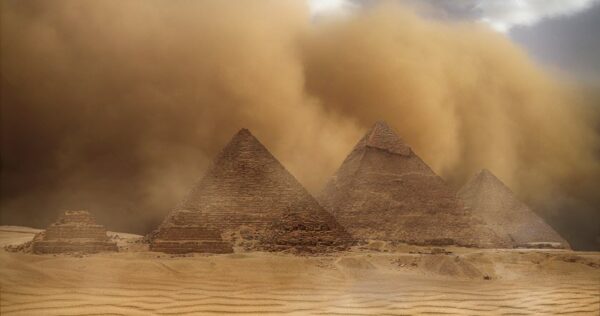 The Pyramids of Giza stand amid a sandstorm, with dust clouds swirling in the background and desert sand covering the ground.