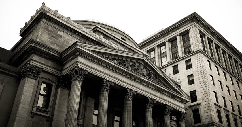 Black and white photo of two large historic buildings with columns and ornate stonework, viewed from a low angle.