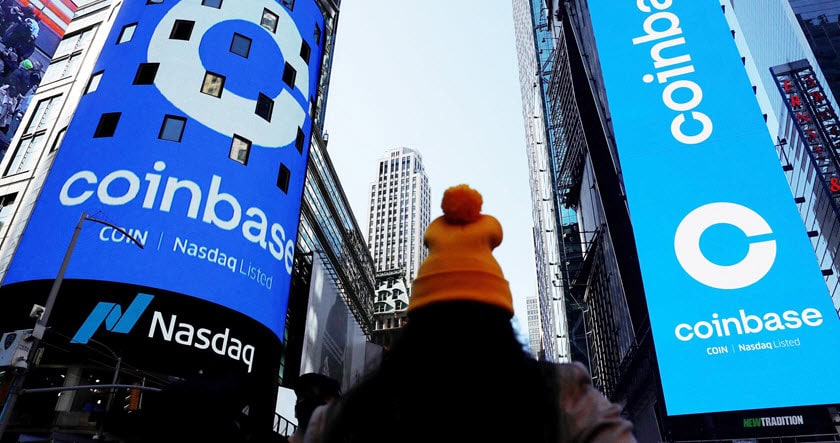 A person faces large digital billboards displaying Coinbase and Nasdaq logos in a cityscape with high-rise buildings.