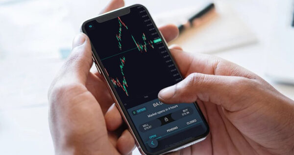 A person holds a smartphone displaying a candlestick chart and trading options on a financial market app.