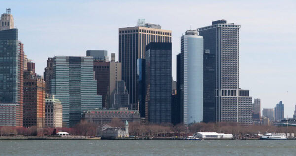 A view of lower Manhattan’s skyline with modern high-rise office buildings and water in the foreground.