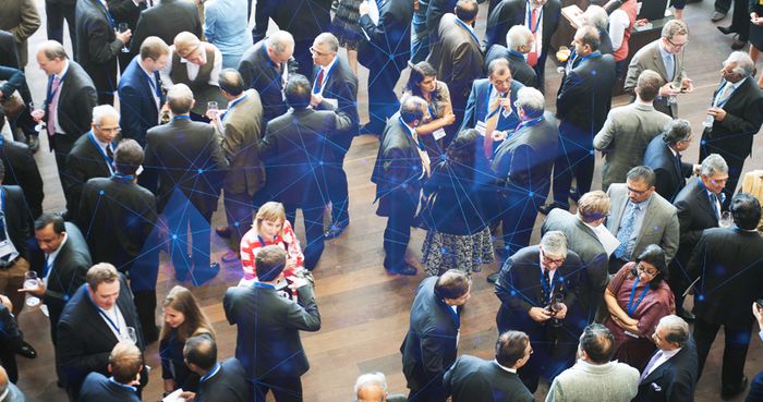 A large group of people in business attire gather and converse at a networking event viewed from above.