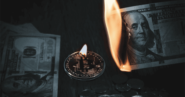 A silver Bitcoin coin and stacks of coins are next to a burning US $100 bill, with more US bills partially visible in the background.