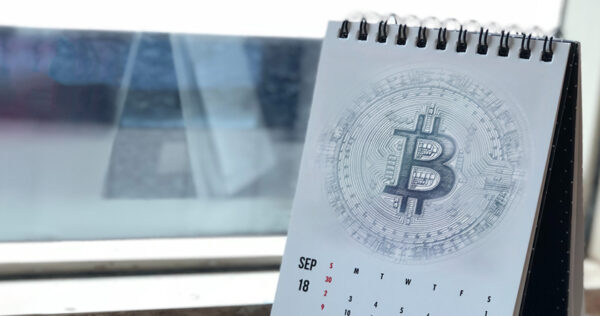A desk calendar displaying September with a large Bitcoin symbol printed on the page, placed by a window.