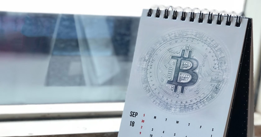 A desk calendar displaying September with a large Bitcoin symbol printed on the page, placed by a window.