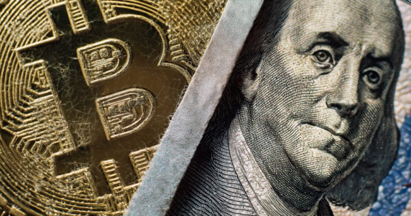 Close-up of a Bitcoin coin next to part of a US hundred-dollar bill featuring Benjamin Franklin’s face.