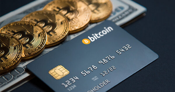 A Bitcoin-branded credit card is placed on top of US dollar bills and several physical Bitcoin coins.