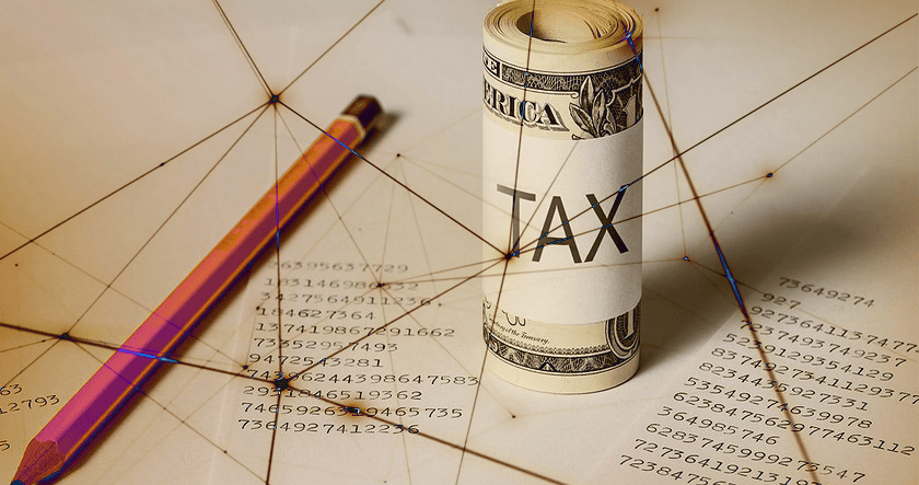 A rolled-up dollar bill labeled "TAX," a pencil, and financial documents with numbers are shown on a table.
