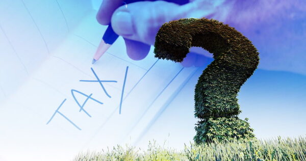 A large question mark-shaped hedge stands in grass; overlaid is a hand writing 