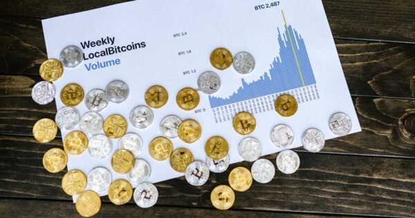 A printed chart showing weekly LocalBitcoins volume with scattered gold and silver bitcoin tokens on a wooden surface.