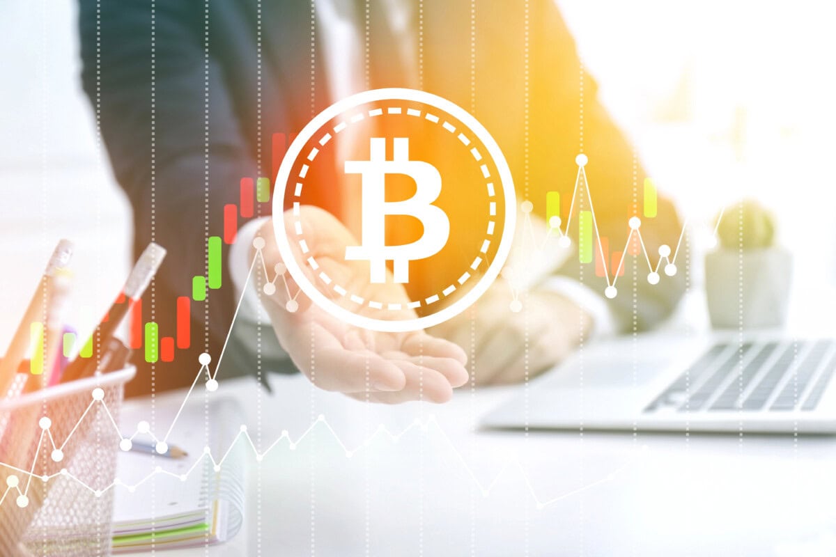 A person in business attire gestures toward a glowing Bitcoin symbol, with digital financial charts and graphs in the background, suggesting cryptocurrency investment or market analysis.
