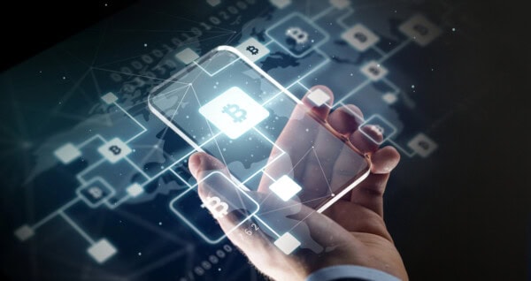 A person holds a transparent smartphone displaying a glowing Bitcoin symbol, with digital blockchain network icons and connections overlaying a world map in the background.