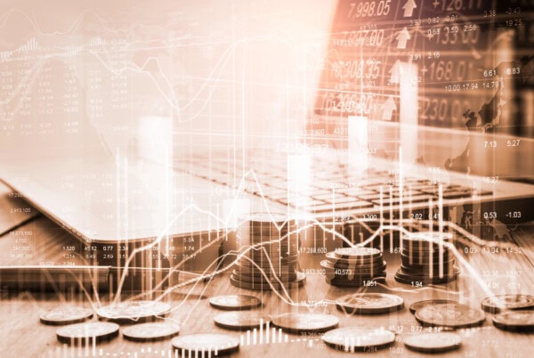 Stacks and scattered coins in front of a laptop keyboard, overlaid with digital financial graphs and stock market data, suggesting concepts of online trading, investment, and financial analytics.