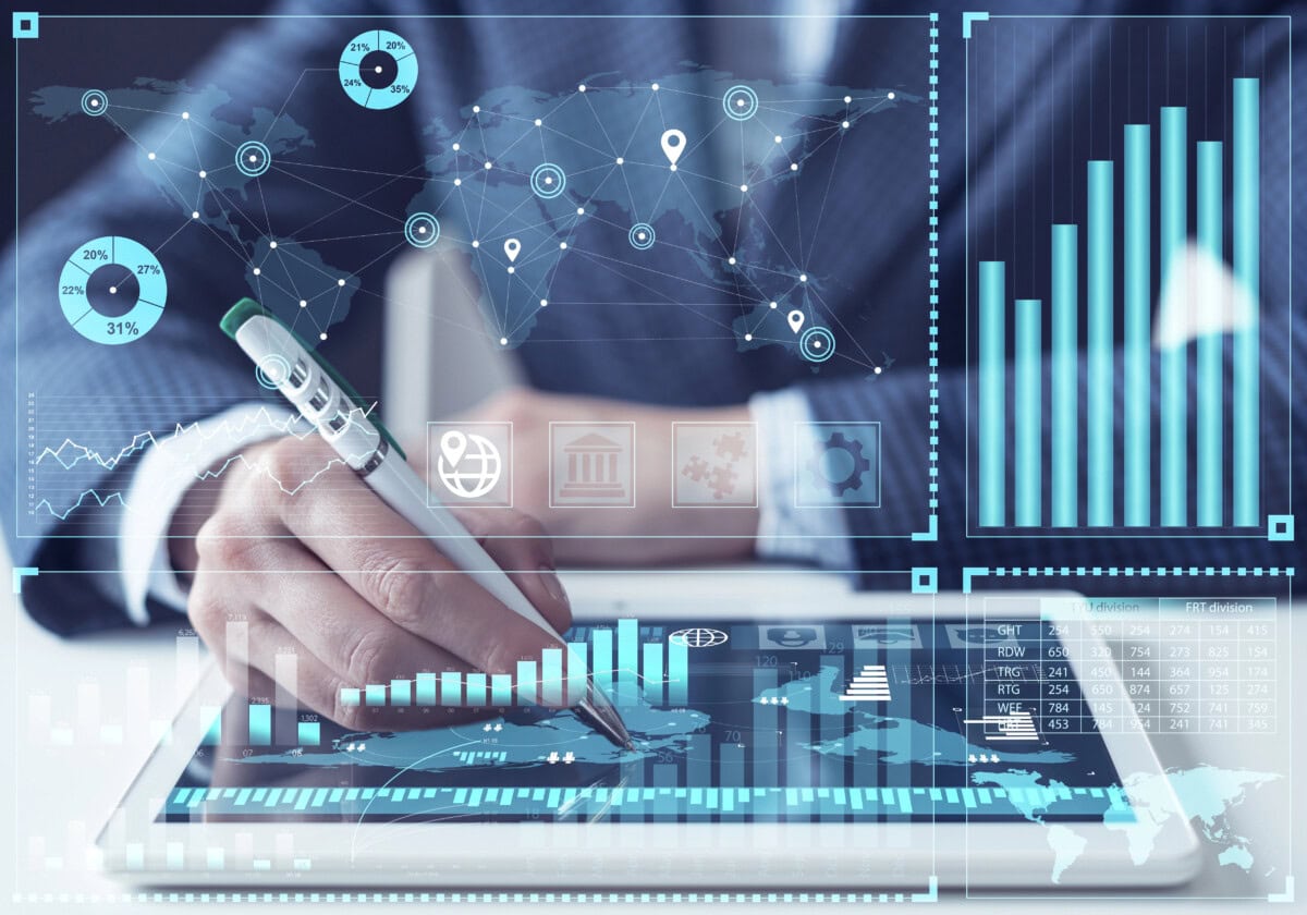 A person in a suit uses a stylus on a tablet displaying digital graphs, charts, and world maps, symbolizing data analysis, global business, and financial technology concepts.