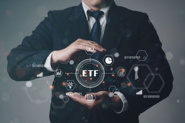 A person in a suit holds their hands around a glowing circle labeled ETF, surrounded by virtual finance icons and hexagons, symbolizing exchange-traded funds and financial technology.