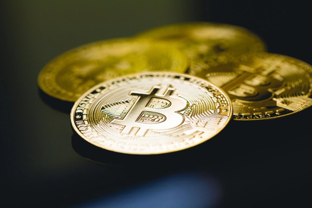 Close-up of shiny gold-colored physical coins with the Bitcoin symbol, placed on a dark surface, representing the concept of cryptocurrency and digital currency.