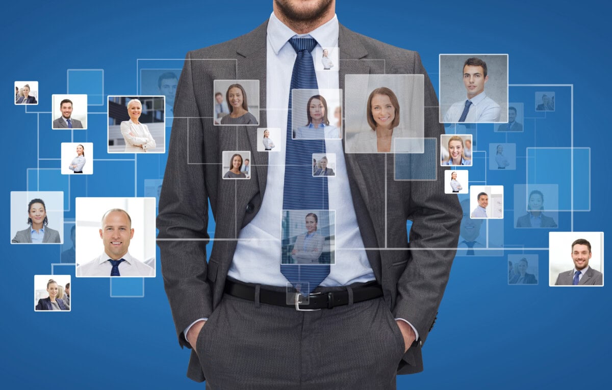 A man in a suit stands with his hands in his pockets against a blue background. Floating transparent rectangles display various headshots of diverse professionals, suggesting networking or a digital business connection.