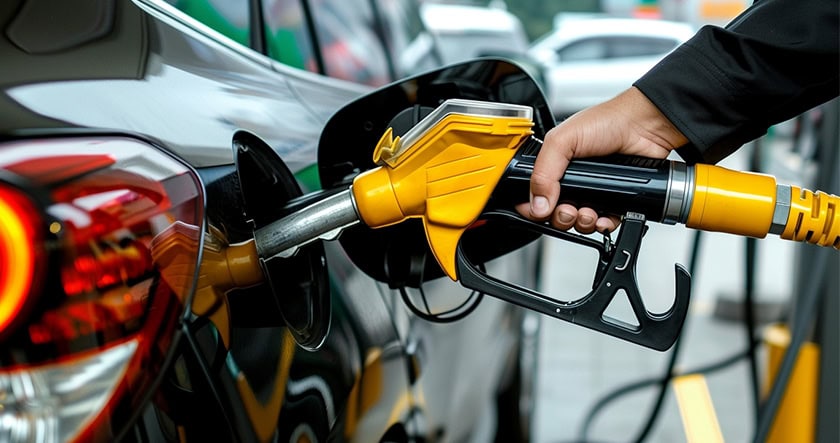 A person is refueling a black car at a gas station, holding a yellow fuel pump nozzle inserted into the vehicle’s gas tank.
