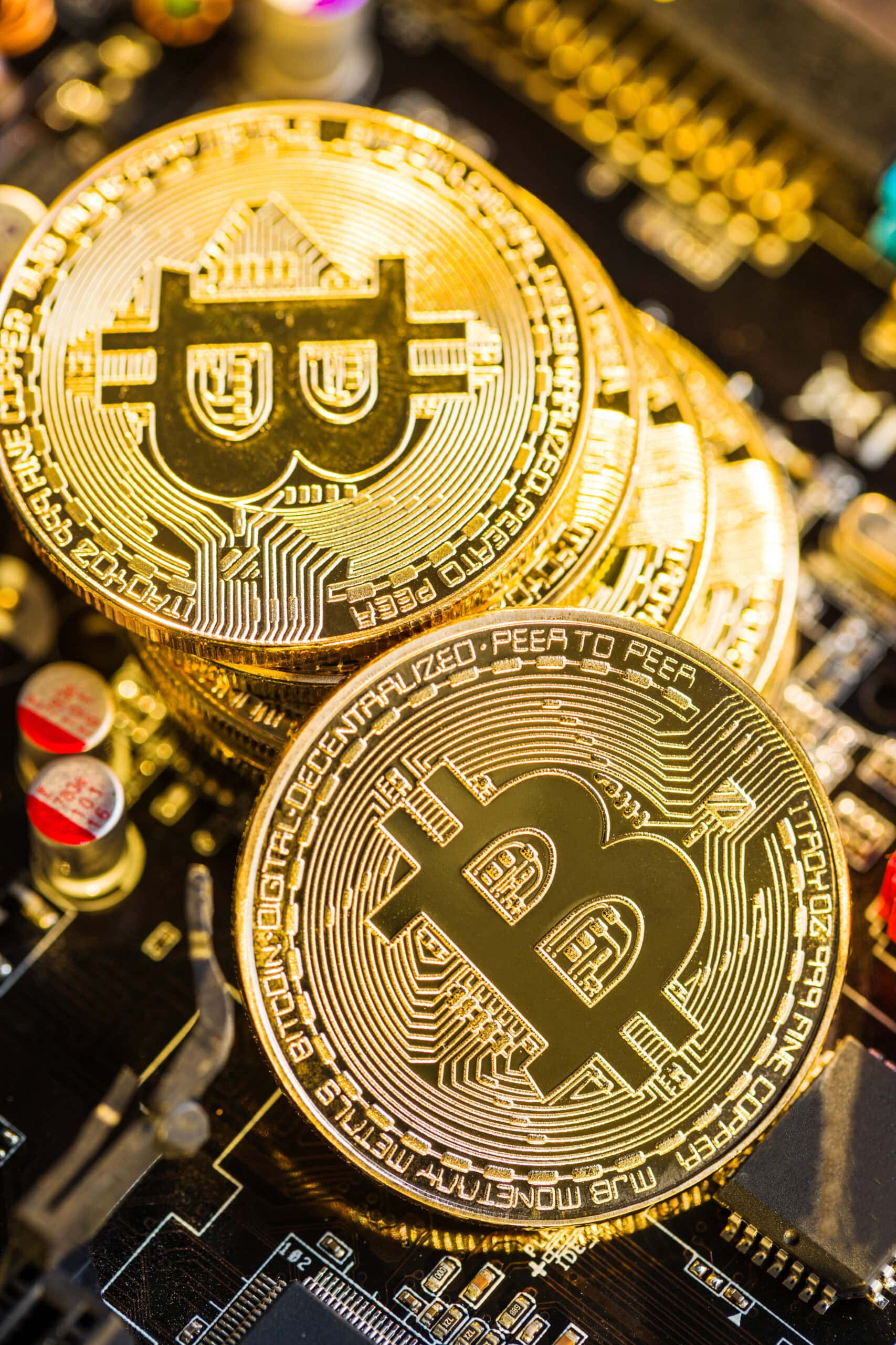 A close-up of several shiny gold bitcoin coins placed on top of a computer circuit board, symbolizing cryptocurrency and digital finance.