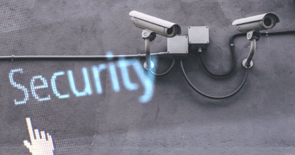 Two security cameras are mounted on a concrete wall near electrical boxes, with the word 