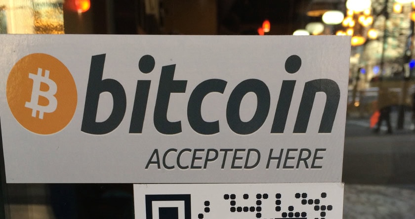 A sign on a window displays the Bitcoin logo and the words "bitcoin accepted here," indicating the business accepts Bitcoin payments.