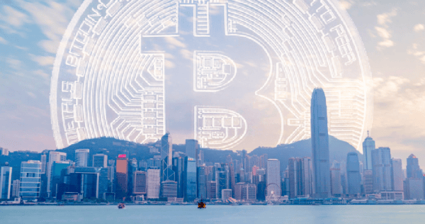 Hong Kong city skyline with a large, digital Bitcoin symbol superimposed in the sky above the skyscrapers.