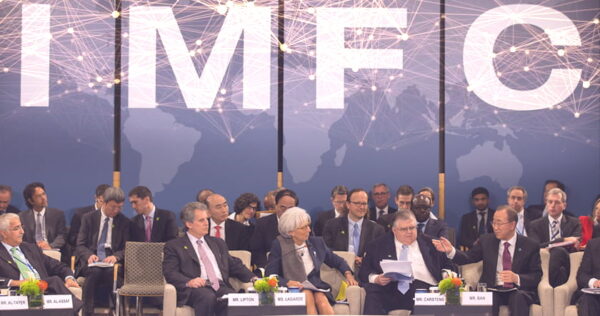 A group of officials sit and discuss on stage at an IMF conference, with a world map and 