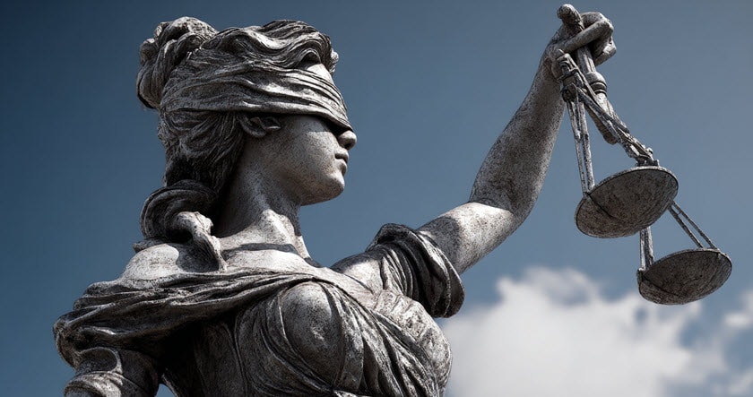 Statue of Lady Justice holding balanced scales and wearing a blindfold, symbolizing impartiality and fairness against a cloudy sky background.