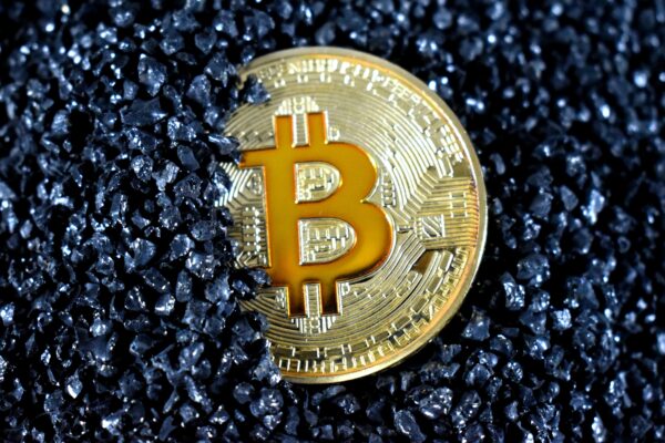 A gold Bitcoin coin partially buried in black, shiny granular stones.