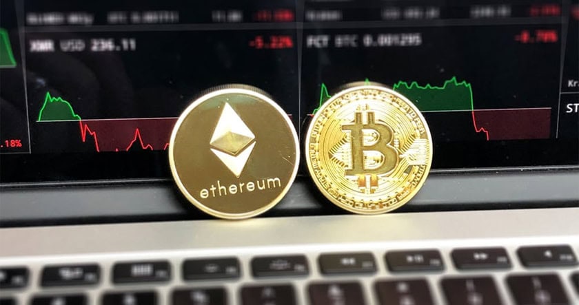 Ethereum and Bitcoin physical coins placed on a laptop keyboard, with a cryptocurrency market chart displayed on the screen in the background.