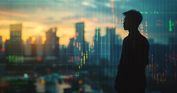 Silhouette of a person standing in front of a city skyline at sunset, with digital financial charts and data graphics overlayed on the image.