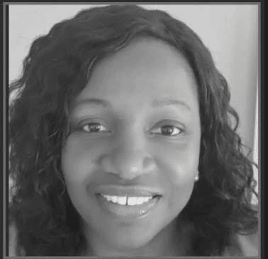 A woman with curly hair smiles at the camera in a black and white portrait.