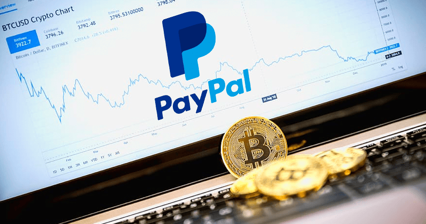 A PayPal logo is displayed on a screen showing a cryptocurrency chart, with Bitcoin coins placed on a laptop keyboard in the foreground.