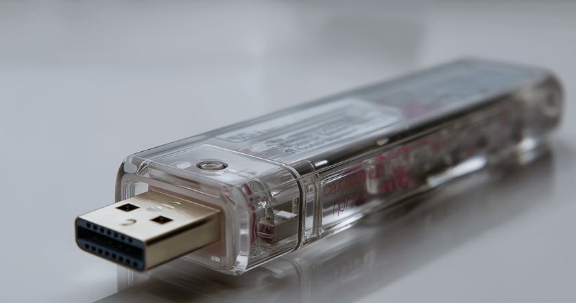 A close-up of a transparent USB flash drive with a visible gold-colored connector, placed on a reflective surface.