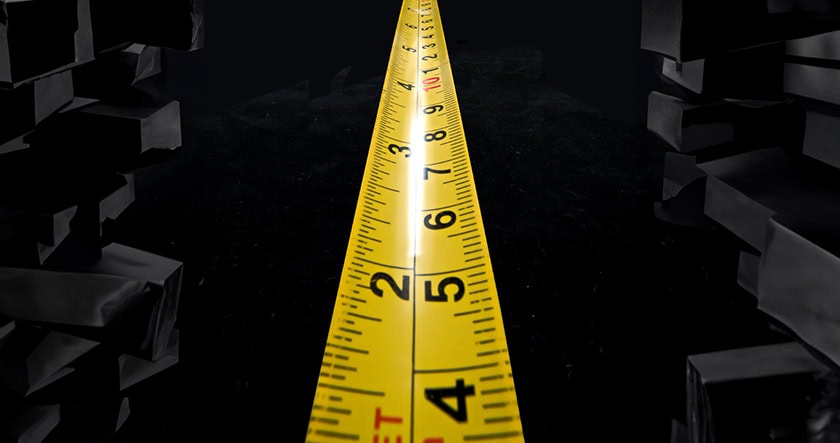 A yellow measuring tape extended forward, surrounded by stacks of black rectangular blocks on both sides, against a dark background.
