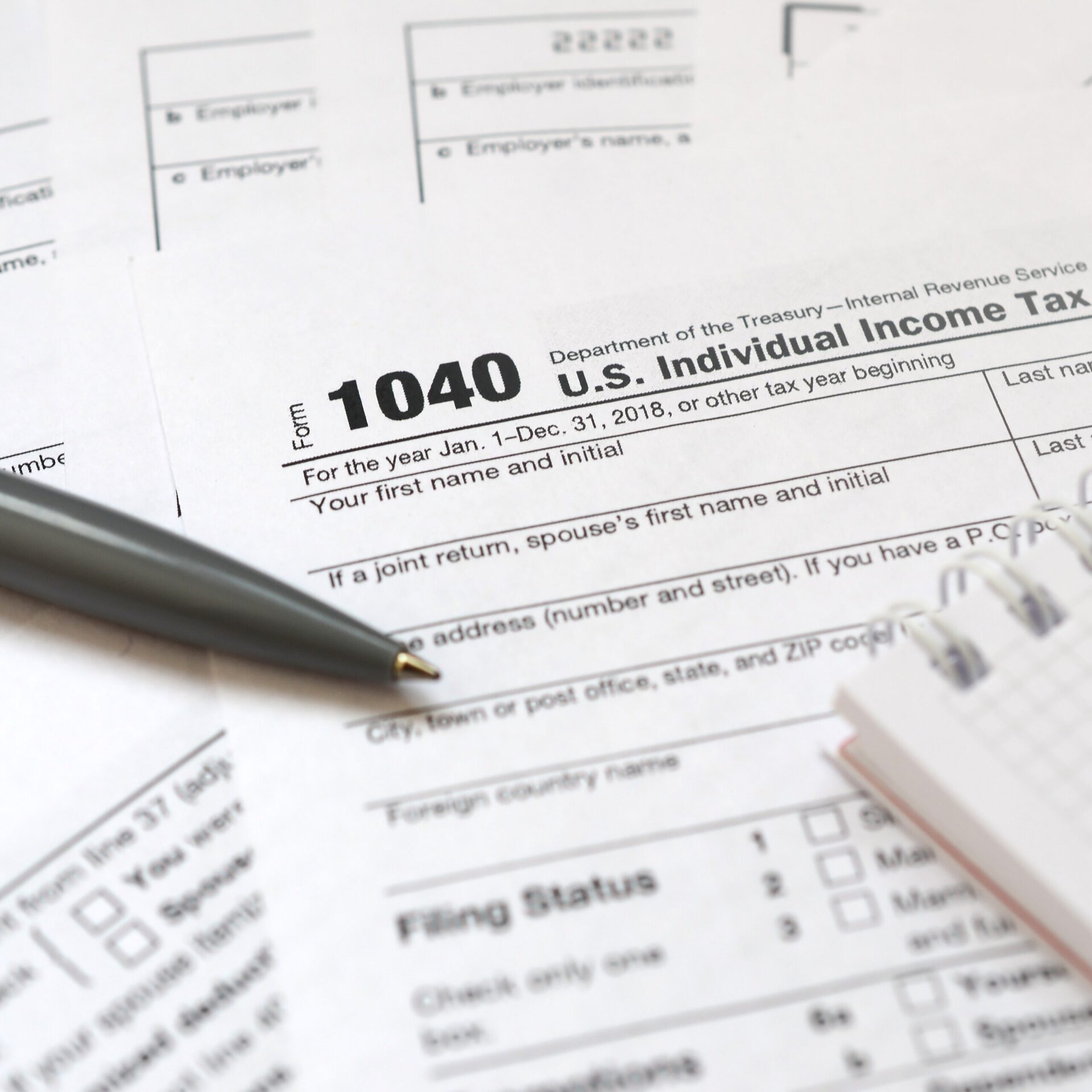 Close-up of a U.S. 1040 Individual Income Tax Return form with a pen resting on top and a notepad on the side, representing tax preparation and financial paperwork.